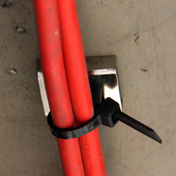 Close-up of magnetic cable tie mount suspending a red cable from a steel gurder