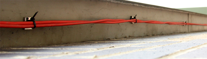 Magnetic cable tie mounts holding thick red cable to underside of a steel gurder